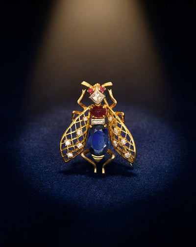 Vintage Van Cleef & Arpels bee brooch with diamond lattice wings, blue sapphire body, and ruby accents in 18k yellow gold, spotlit on navy velvet
